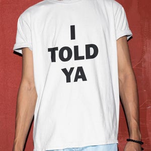 May include: White t-shirt with black text that reads "I TOLD YA".