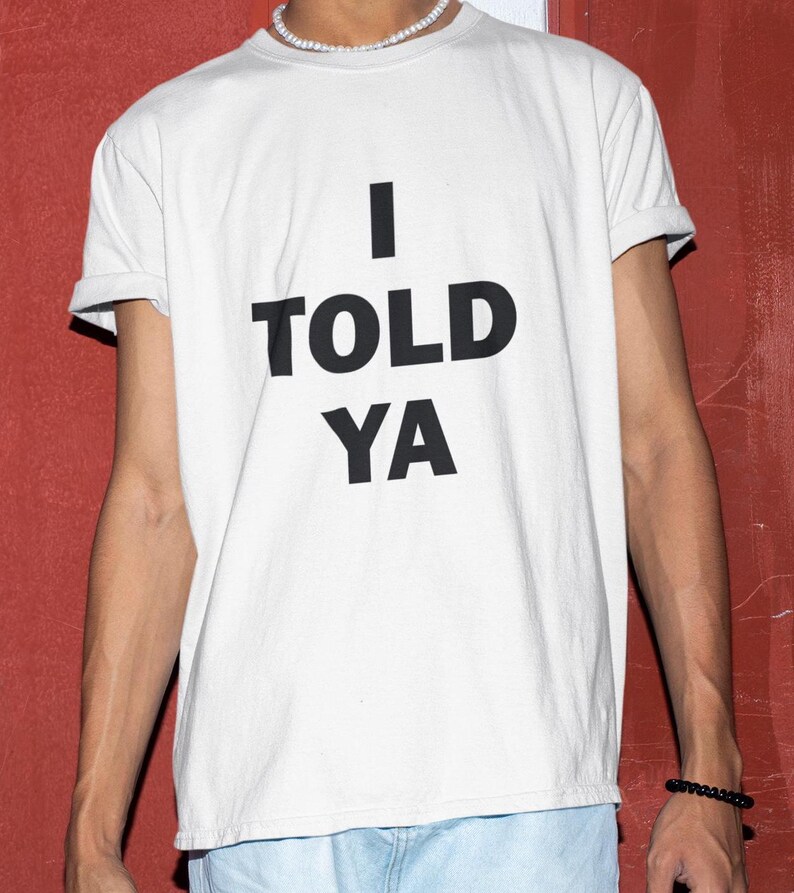 May include: White t-shirt with black text that reads "I TOLD YA".