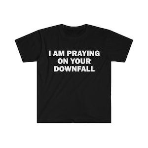 May include: Black t-shirt with white text that reads "I AM PRAYING ON YOUR DOWNFALL".