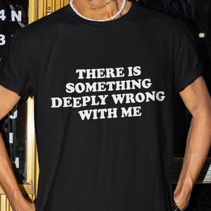 Op de afbeelding: Zwart T-shirt met witte tekst die "Er is iets diep mis met mij" zegt.