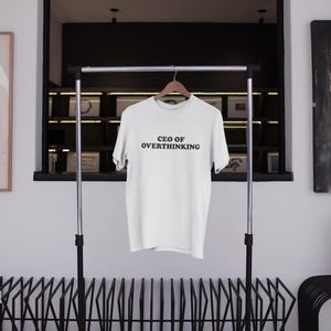 May include: White t-shirt with the text "CEO of Overthinking" printed in black on the front.