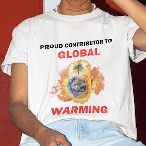 May include: White t-shirt with the text "Proud Contributor to Global Warming" in black and red letters. The shirt features a graphic of a burning Earth with a tree on top.