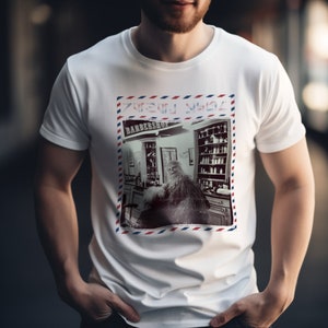 May include: White t-shirt with a vintage-style image of a man with a long beard sitting in a barbershop chair. The image is framed with a red, white, and blue border and includes the text "Barber Shop".