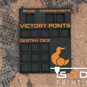 May include: Black plastic game organizer with compartments for storing game pieces. The organizer has labels for "Round", "Command Points", "Victory Points", and "Destiny Dice". It also features a small orange duck logo.