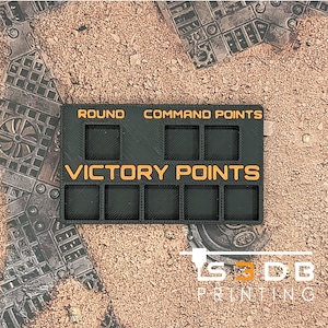 May include: Black and orange plastic tracker for a board game. It has spaces for tracking round, command points, and victory points.