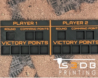 May include: A black and orange 3D printed game tracker with spaces for two players. The tracker has spaces for round, command points, and victory points.