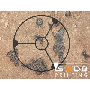 Peut inclure: Un cadre circulaire noir avec trois rayons, reposant sur une surface sablonneuse. Le cadre est entouré de petits morceaux de métal dispersés. Le texte "S3DB PRINTING" est visible dans le coin inférieur droit de l'image.