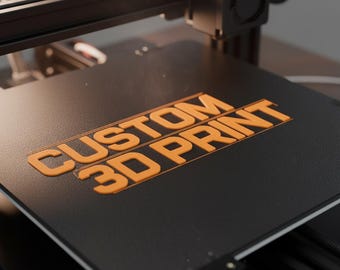 May include: A close-up of a 3D printer with the words "CUSTOM 3D PRINT" in orange on a black surface. The printer has a black frame and a fan.