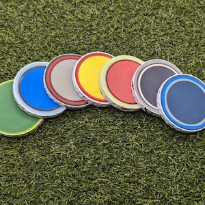 May include: Seven round, colorful, paper discs with white borders. The discs are arranged in a semi-circle on a green surface.