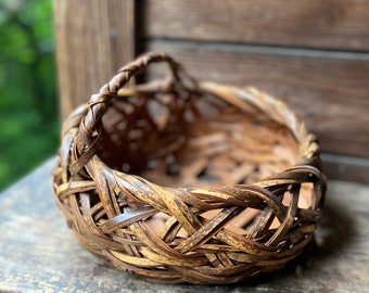 May include: A woven basket made of natural brown and tan bamboo. The basket has a rounded shape with a single handle.