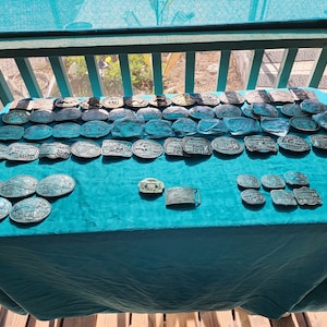 May include: A collection of over 50 vintage belt buckles, mostly in shades of silver and bronze, displayed on a teal tablecloth. The buckles feature various designs, including geometric patterns, animals, and abstract shapes.