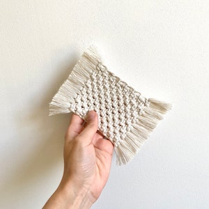 Puede incluir: Un posavasos de crochet blanco con flecos alrededor de los bordes.