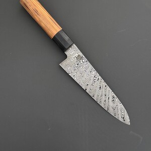 May include: A Japanese-style chef's knife with a patterned blade and a wooden handle. The blade has a unique swirling design. The handle is light brown with a black bolster. The knife is designed for precision cutting.