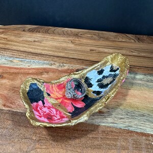 Könnte beinhalten: Eine goldene Ring Schale mit einem floralen und tierischen Muster. Die Schale ist aus Harz und hat einen einzigartigen, handgefertigten Look.