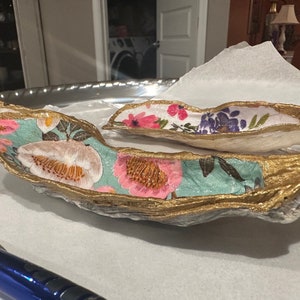 Könnte beinhalten: Zwei dekorative, goldbemalte, blattförmige Schalen mit Blumenmustern. Die größere Schale hat einen türkisfarbenen Hintergrund mit rosa und weißen Blumen. Die kleinere Schale hat einen weißen Hintergrund mit rosa, violetten und grünen Blumen.