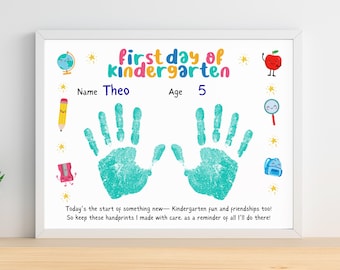 May include: A framed print with the words "first day of kindergarten" in colorful letters. It includes a child's name, age, and handprints in teal. The print is decorated with school-themed illustrations and a quote about kindergarten.