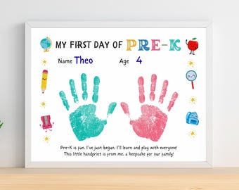 May include: A framed print with the text "MY FIRST DAY OF PRE-K" and the name "Theo" and age "4". The print features teal and pink handprints, along with colorful illustrations of school-related items. The text "Pre-K is fun..." is also included.
