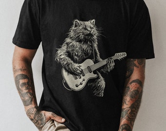 May include: Black t-shirt featuring a white graphic of a cat playing an electric guitar.
