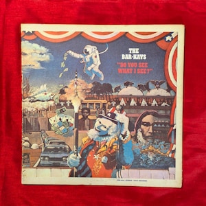May include: Vintage album cover for The Bar-Kays' "Do You See What I See?" featuring a colorful, surreal illustration. An astronaut, a clown, and a Native American are depicted in a patriotic, Americana-themed design with a blue, red, and white color scheme.