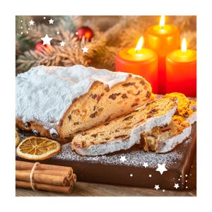 Puede incluir: Un pastel stollen, espolvoreado con azúcar glas, se corta para revelar frutas secas. El pastel descansa sobre una tabla de madera, junto con velas encendidas y palitos de canela, creando una escena festiva.