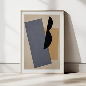 Puede incluir: Impresión artística abstracta enmarcada con formas geométricas en tonos apagados. Una forma rectangular gris grande se encuentra junto a un rectángulo más pequeño de color beige. Una forma negra curva se superpone a las otras formas. La obra de arte se exhibe en una pared blanca.