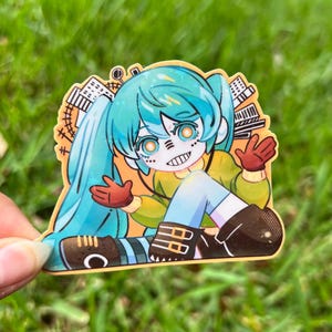 May include: A colorful sticker featuring an anime-style character with turquoise pigtails, orange eyes, and a stitched mouth. The character wears a yellow top, blue shorts, and brown boots. The sticker has a cityscape design and red gloves.