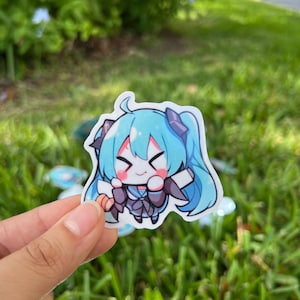K&ouml;nnte beinhalten: Ein blauer und schwarzer Anime-Charakter-Aufkleber mit wei&szlig;em Hintergrund. Der Charakter hat langes blaues Haar, schwarze Augen und einen rosa Rouge auf den Wangen. Sie tr&auml;gt ein schwarz-wei&szlig;es Outfit und h&auml;lt ein wei&szlig;es Objekt in ihrer rechten Hand.