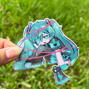 May include: A sticker featuring a teal-haired anime character with a black and teal outfit, pink accents, and a megaphone. The character is sitting with pink lines around them.