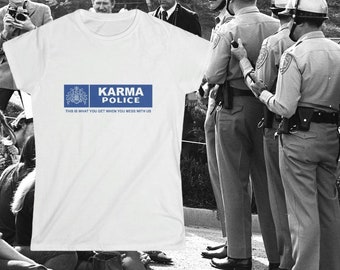 Peut inclure: T-shirt blanc avec l'inscription "Karma Police" en bleu, un blason et la phrase "This is what you get when you mess with us." L'image est présentée sur un fond en noir et blanc avec des personnes et des policiers.