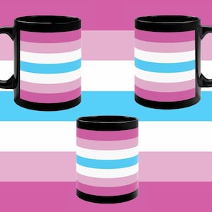 May include: Three black mugs with a transgender pride flag design. The flag has five horizontal stripes: light pink, white, light blue, white, and light pink.