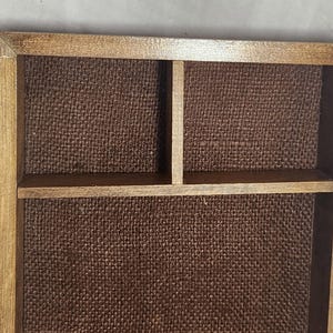 Puede incluir: Una bandeja rectangular de madera con acabado marr&oacute;n medio, que presenta un forro de tela texturizada en color marr&oacute;n oscuro. El interior est&aacute; dividido en tres secciones distintas por finos tabiques de madera, creando un &aacute;rea grande y dos compartimentos.