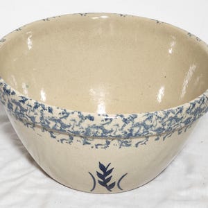 May include: A large, off-white stoneware bowl with a blue, speckled rim and a blue leaf design. The bowl has a wide, open shape, perfect for mixing or serving. The stoneware has a rustic, vintage aesthetic.
