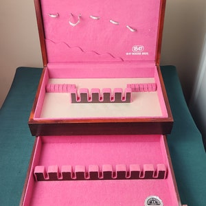 May include: A wooden silverware chest with a pink velvet interior. The chest has a drawer and a hinged lid. The lid has a label that reads "1847 Rogers Bros."