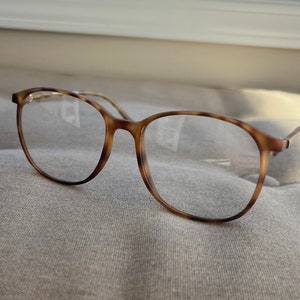 May include: Tortoise shell eyeglasses with round frames and clear lenses.