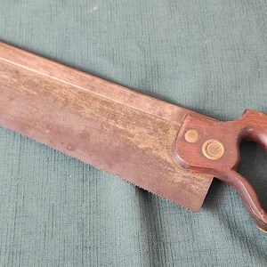 May include: A vintage hand saw with a wooden handle and brass accents. The blade is rusty and has a patina.