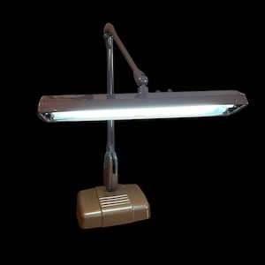May include: A brown metal desk lamp with a long, adjustable arm and a fluorescent light fixture. The lamp has a brown base and a silver-colored arm.