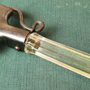May include: A vintage glass and metal ice scraper with a metal handle and a clear glass blade. The handle has a metal loop for hanging.
