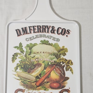 May include: White rectangular metal sign with a handle, featuring a vintage illustration of vegetables and the text "D.M. Ferry & Cos Celebrated Seeds For Sale Here."