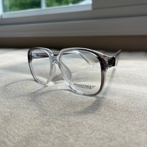 May include: Clear plastic framed glasses with a black "Mainstreet Collection" logo on the right temple.
