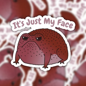 May include: A sticker featuring a cartoon red frog with a grumpy expression. The text "It's Just My Face" is written above the frog.