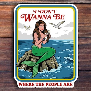 May include: A sticker featuring a mermaid sitting on a rock in the ocean, holding a fish. The sticker has the text "I DON'T WANNA BE WHERE THE PEOPLE ARE" in red and white. The mermaid has green scales and brown hair.
