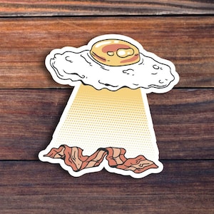 May include: A cartoon illustration of a fried egg flying in a UFO over a pile of bacon. The egg has a yellow yolk and a white, fluffy cloud-like shape. The bacon is brown and crispy.