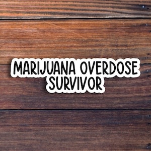 May include: White sticker with black text on a brown wooden background. The text reads "Marijuana Overdose Survivor".