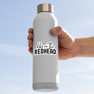 May include: A white stainless steel water bottle with a black sticker that says "dibs on the redhead".