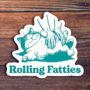 May include: A teal blue sticker with a cartoon illustration of a cat being rubbed on its belly by two hands. The text "Rolling Fatties" is printed below the cat.