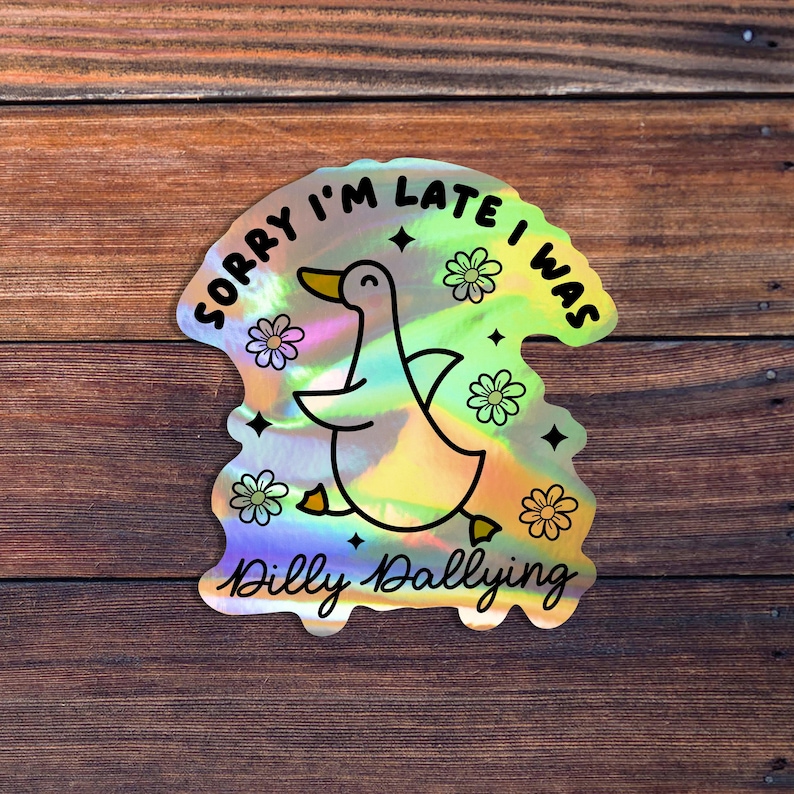 May include: A holographic sticker with a cartoon duck and the text "Sorry I'm late I was dilly dallying". The duck is yellow and has a black outline. The text is black and surrounded by a rainbow-colored background.