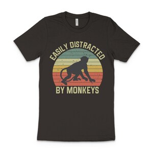 May include: A dark grey t-shirt with a vintage-style graphic of a monkey and the text "Easily Distracted By Monkeys".