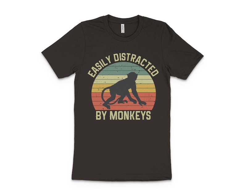 May include: A dark grey t-shirt with a vintage-style graphic of a monkey and the text "Easily Distracted By Monkeys".