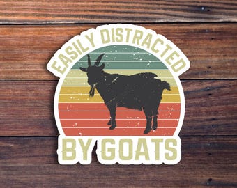 Może przedstawiać: Naklejka w stylu vintage z czarną sylwetką kozy i tekstem "Easily Distracted By Goats". Tło to czerwony, pomarańczowy i żółty zachód słońca.