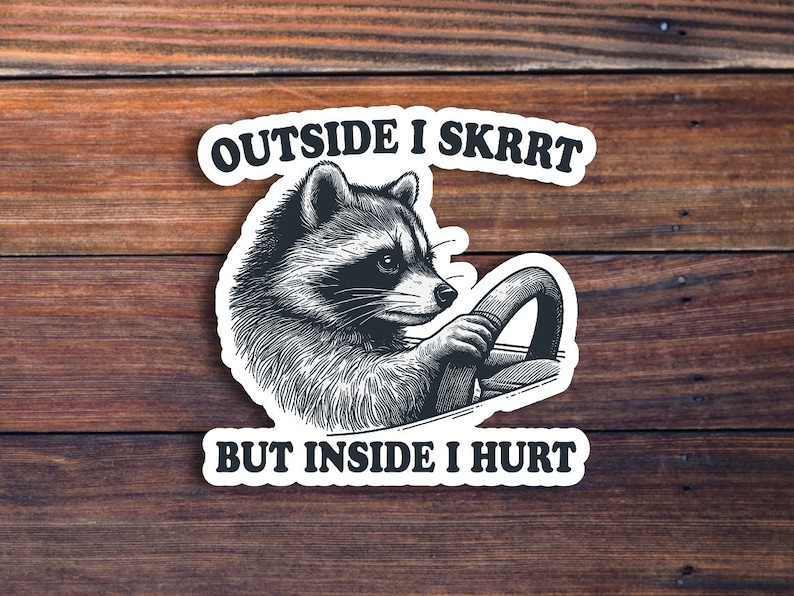 May include: A black and white sticker with a raccoon driving a car. The sticker says "Outside I Skrrt But Inside I Hurt."